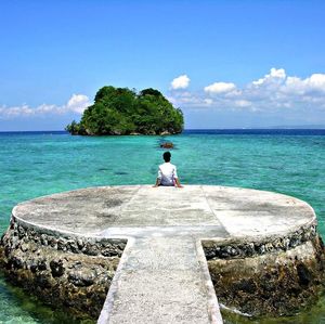 Rear view of woman sitting on rock by sea