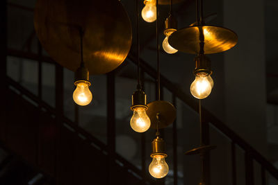 Close-up of illuminated light bulb hanging from ceiling