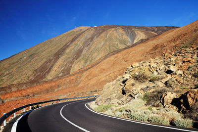 Empty road along rocky landscape against blue sky
