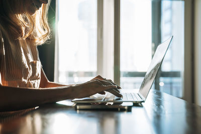 Crop photo of blonde woman with long hair working on laptop phone at home, remote work