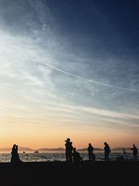 Silhouette people on beach against sky during sunset