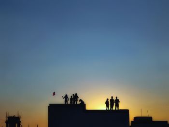 Silhouette people on building against sky during sunset