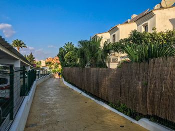 Footpath amidst buildings against blue sky