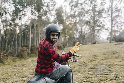 Smiling male biker gesturing while exploring forest on motorcycle