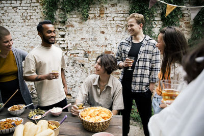 Male and female friends talking to each other holding drink glass at garden party in back yard