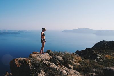 Woman standing on rock by sea against clear sky