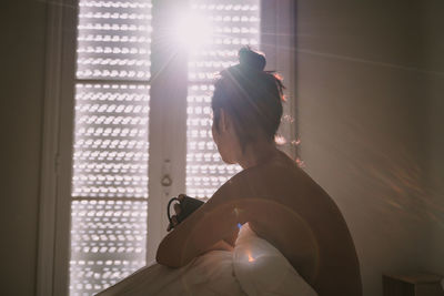 Rear view of woman holding window at home