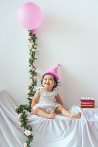 Portrait of cute girl with pink balloons against wall