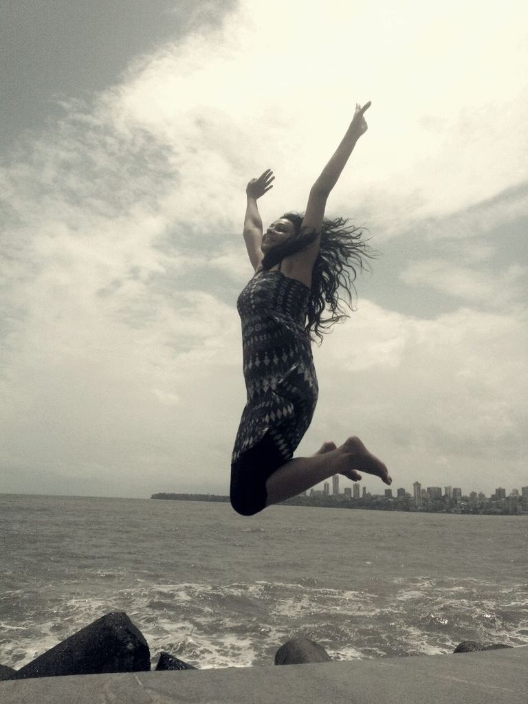 full length, sea, mid-air, jumping, sky, water, lifestyles, leisure activity, arms outstretched, freedom, enjoyment, beach, cloud - sky, horizon over water, carefree, arms raised, flying, fun