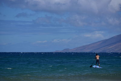 Rear view of shirtless man paddleboarding at sea against sky