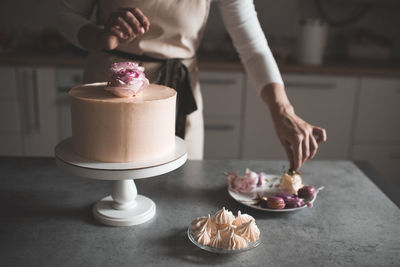 Woman making cake decorating with flower roses staying on kitchen table close up at home. 