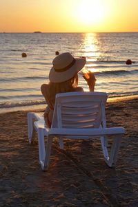 Rear view of woman relaxing on lounge chair at beach during sunset