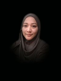 Portrait of smiling woman wearing hijab against black background