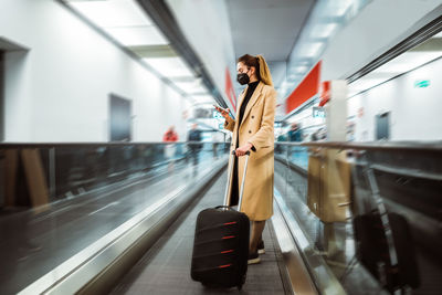 Woman wearing mask standing at airport with luggage