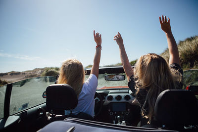 Rear view of women sitting in car against sky