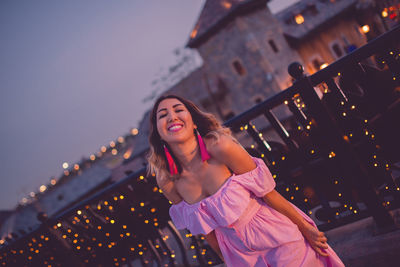 Cheerful fashionable woman standing in city during sunset