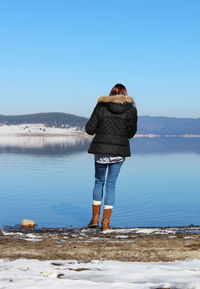 Rear view of woman standing on shore against clear sky
