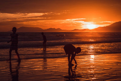 Silhouette men standing at beach during sunset