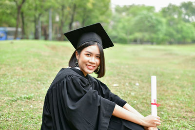 Side view portrait of young woman sitting in graduation gown at park