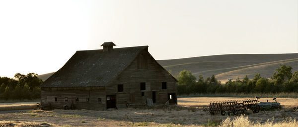 Abandoned house by barn against clear sky