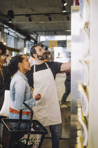 Mature salesman with female customer standing at delicatessen