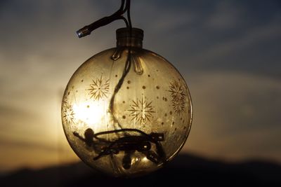 Close-up of light bulb hanging against sky during sunset