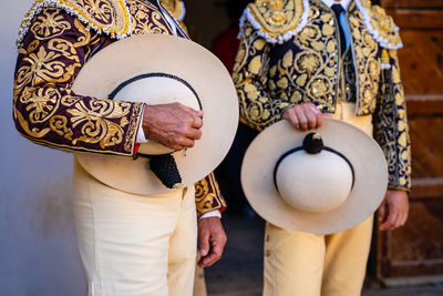Crop unrecognizable bullfighters in traditional costume decorated with embroidery holding hats and preparing for corrida festival