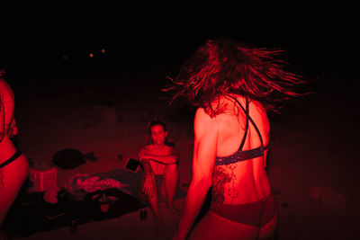 Group of young women having fun at a lakeside party at night with a red light