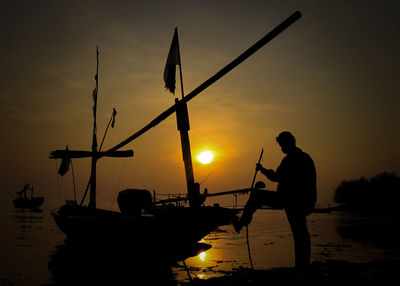 Silhouette men fishing in sea against sky during sunset