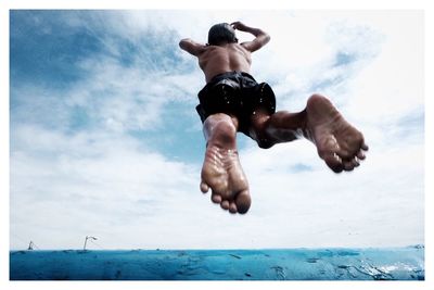 Low angle view of man jumping in sea against cloudy sky