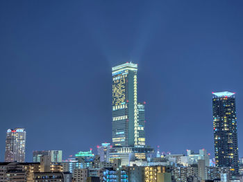 Illuminated cityscape against clear blue sky at night