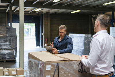 Young male professional discussing over digital tablet with colleague in factory