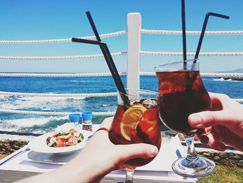 Cropped hands toasting drinks at beach on sunny day