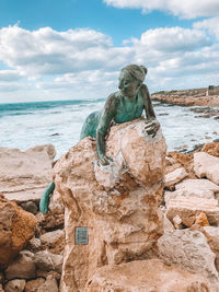 Statue on rock at beach against sky