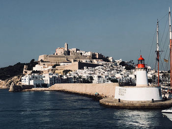 Sailboats in sea by buildings against clear sky