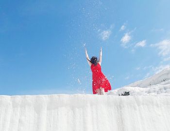 Woman throwing snow against blue sky