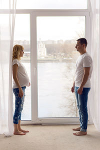 Pregnant woman standing with her husband next to the window