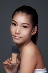 Close-up of young woman with beauty product against gray background