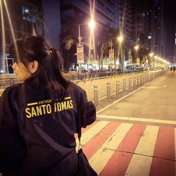 Rear view of woman standing on city street at night