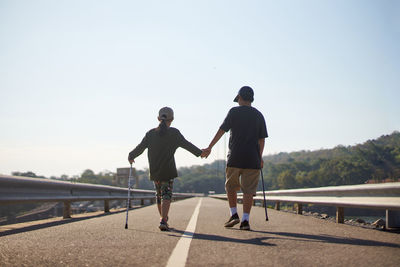 Full length rear view of sibling walking against clear sky