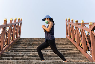 Full length of woman in medical mask doing stretching on the stairs