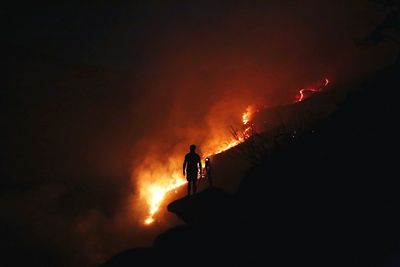 Silhouette man standing with camera against forest fire