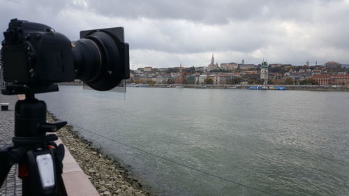 Camera by river against cloudy sky