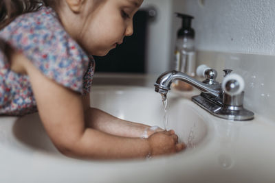 Side view of young girl washing hands in sink with soap