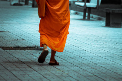 Low section of man wearing orange traditional clothing walking on footpath