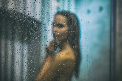 Side view of young woman bathing in bathroom seen through glass