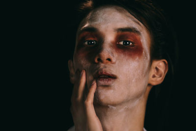 Close-up portrait of young man with halloween make-up against black background