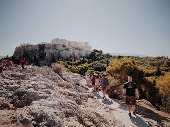 People walking on rocks against clear sky