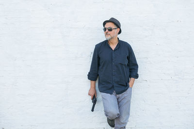 Man wearing sunglasses holding gun against white wall