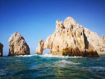 Rock formations in sea against clear blue sky